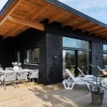 Modern villa with wooden terrace, seating group, and lounge chairs. Black cladding and large windows.