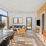 Living and dining area with wooden floor, large windows, and modern furnishings.