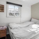 Bedroom with bed, window, and wooden shelf on the wall.