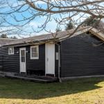 Black wooden house with white doors and windows. Lawn and trees in the background.