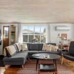 Living room with sofa, armchair, and fireplace. Wooden floor and window view.