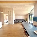 Living area with dining table, sofa, and kitchen. Wooden ceiling and walls. TV and bedroom in background.