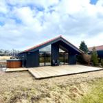 Modern villa with wooden terrace and hot tub. View of the garden and sky.