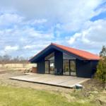 Modern villa with wooden terrace and large glass area under red roof.