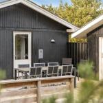 Holzterrasse mit Tisch und Stühlen vor einem schwarzen Holzhaus mit Grill.