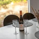 Tisch mit Weinglas, Flasche und Vasenblumen vor Fenster