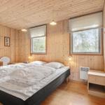 Schlafzimmer mit Holzwandverkleidung, Bett, zwei Fenstern und Nachttisch.