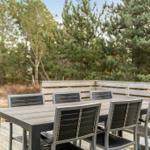 Holzterrasse mit Tisch und sechs Stühlen, umgeben von Bäumen.