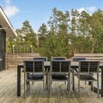 Terrasse mit Tisch, Stühlen und Grill. Hintergrund: Wald und Himmel.