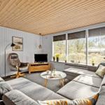 Wohnzimmer mit Sofa, Sessel und TV. Große Fenster mit Blick nach draußen.