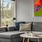Grauer Sofa mit Kissen, runder Tisch und Fensterblick auf Wald.