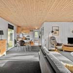 Wohnbereich mit Sofa, Sessel und TV. Küche im Hintergrund. Holzdecke und weiße Wände.