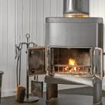 Holzofen mit brennendem Feuer und Werkzeug neben einem Metallfass.