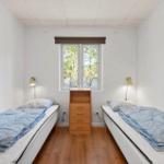 Zwei Einzelbetten mit blauen Decken, Holzschrank und Fenster mit Blick auf Bäume.