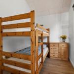 Ein Schlafzimmer mit einem Holzbett und einem Schrank. Ein Fenster und eine Tür sind sichtbar.