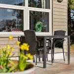 Terrasse mit Tisch und zwei Stühlen vor einem Haus mit Fenster.