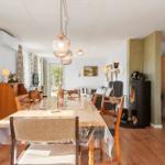 Esszimmer mit Esstisch, Stühlen und Kaminofen. Wohnbereich mit Sofa und Bücherregal.