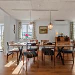 Esszimmer mit Holztisch, Stühlen und Fenstern mit Vorhängen.