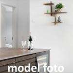 Küche mit dunklem Arbeitsplatz, Weinflasche und Gläsern, Wandregal mit Pflanze und Deko.