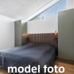 Schlafzimmer mit Doppelbett, Holzfußboden und großem Fenster. Zwei Schränke und Holzpaneel an der Wand.