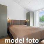 Schlafzimmer mit Bett, Kleiderschrank und Fensterblick auf Wald.