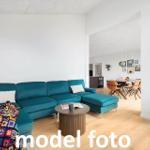 Ein Wohnzimmer mit türkisfarbenem Sofa, Holzboden und Essbereich im Hintergrund.