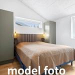 Schlafzimmer mit Bett, Kleiderschrank und Fenstern.