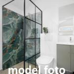 Bad mit Dusche, Waschbecken und Toilette. Duschwand mit Marmoroptik.