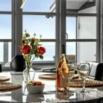 Runder Tisch mit Wein, Blumen und Meerblick durch Fenster
