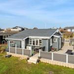 Ein graues Ferienhaus mit Terrasse und Garten. Möbel und Pflanzen sind draußen platziert.
