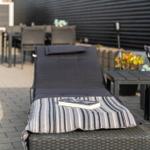 Terrasse mit Liegen, Tisch und Pflanzen. Buch liegt auf einer Decke.