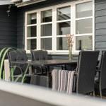 Terrasse mit Tisch und Stühlen vor grauem Haus mit Fenster.