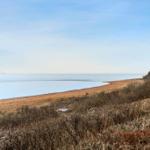 Strand mit sandigem Ufer und ruhigem Meer unter blauem Himmel.