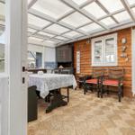 Terrasse mit Tisch, Stühlen und Holzwand. Durchgang ins Wohnzimmer.