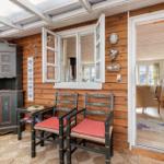 Terrasse mit Holzwand, zwei Stühlen und einem Schrank. Durchgang in Wohnzimmer mit Sofa.