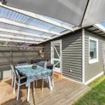 Terrasse mit Tisch, Stühlen und Sonnenschutz neben grauem Haus mit Garten.