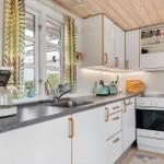 Küche mit weißen Schränken, Edelstahlspüle und Fenster mit Vorhängen.