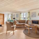 Wohnzimmer mit Holzdecke, Kamin und Sofa. Fenster mit Vorhängen und Wandbilder.