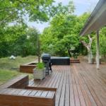 Holzterrasse mit Grill, Whirlpool und Sitzgelegenheiten im Grünen.