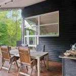 Terrasse mit Tisch, Stühlen und Grillplatz vor schwarzem Holzhaus mit Fenstern.
