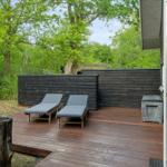 Terrasse mit zwei Liegen und Holzgeländer im Grünen.