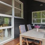 Terrasse mit Holztisch, Stühlen und Blumen. Fenster zeigen den Innenraum.