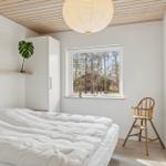 Schlafzimmer mit weißem Bett, Holzdecke und Fensterblick auf Bäume.