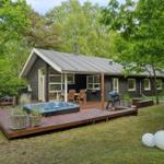 Holzterrasse mit Whirlpool, Grill und Sitzgelegenheiten um eine moderne Hütte herum.