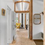 Hallway with wooden floor and beams, view into living area with yellow seating and fireplace.