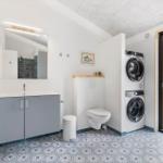 Bathroom with washing machine, toilet, and mirror. Blue tiles on walls.