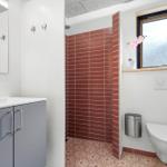 Bathroom with shower, sink, and toilet. Red tiles and window with flower.
