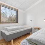 Room with two beds, window view of forest and wooden floor.