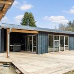 Modern wooden cabin with terrace and grill area. Large window front. Surrounded by trees.