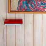Red wall lamp under framed artwork on wood panel wall